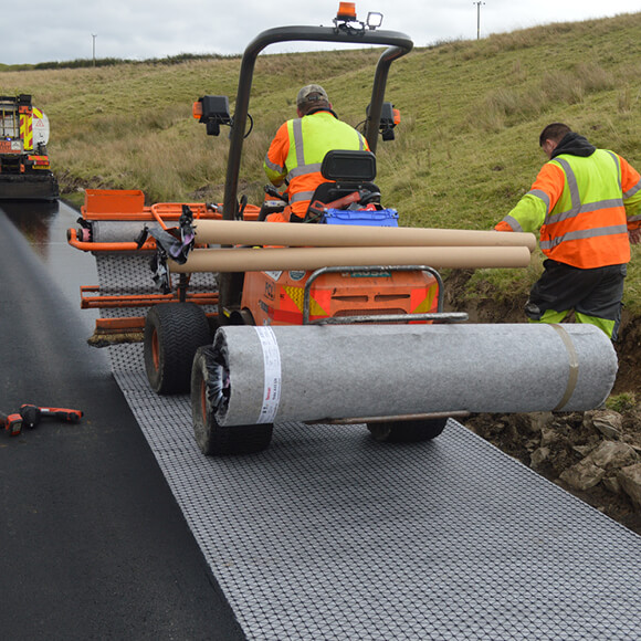 Two construction workers using a construction vehicle to install an asphalt interlayer